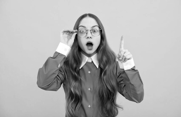 Shocked teenage girl in eyeglasses got genius idea keeping raised finger yellow background, clever - Φωτογραφία, εικόνα