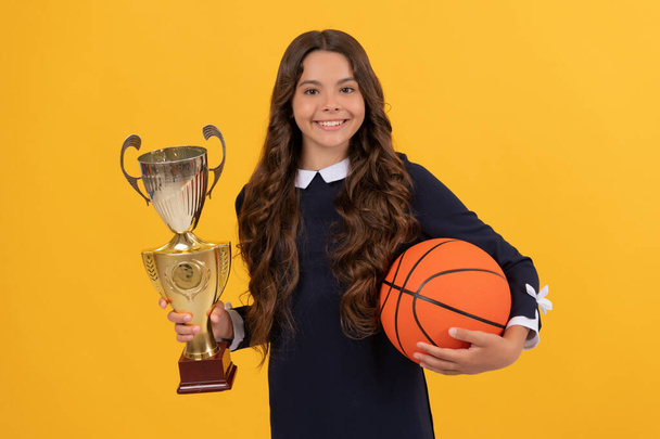 Mutlu çocuk basketbol topunu tutuyor ve sarı arka planda şampiyon kupası, zafer - Fotoğraf, Görsel