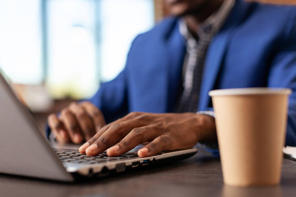 Close-up van de zakenman met behulp van laptop toetsenbord en kopje koffie op kantoor - Foto, afbeelding