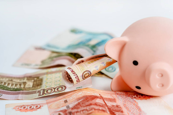 Piggy bank and Russian banknotes on a white background. The concept of accumulation and storage of money - 写真・画像