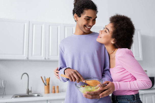Usmívající se africký Američan drží misku se salátem v blízkosti přítelkyně doma  - Fotografie, Obrázek