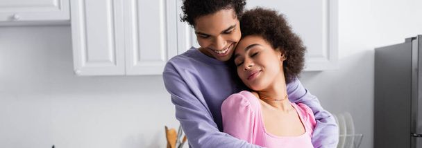 Positive african american man hugging girlfriend at home, banner  - Photo, Image
