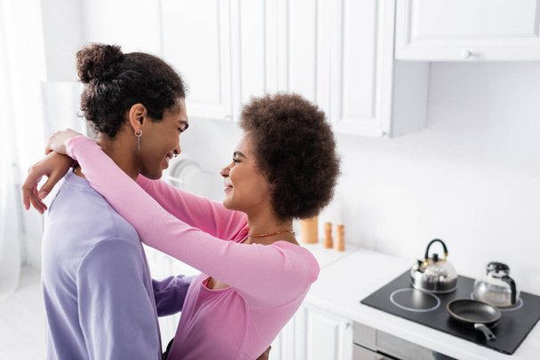 Side view of african american woman embracing young man in kitchen  - Foto, Imagem
