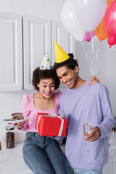 Happy african american couple with cake, champagne and gift in kitchen  - Фото, зображення
