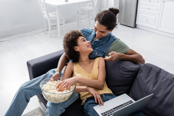 Young african american couple talking near popcorn and laptop at home  - Fotografie, Obrázek