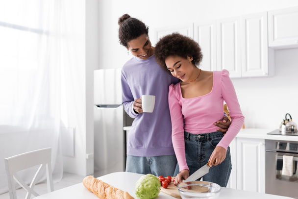 African american man holding cup near girlfriend cooking salad at home  - Foto, immagini
