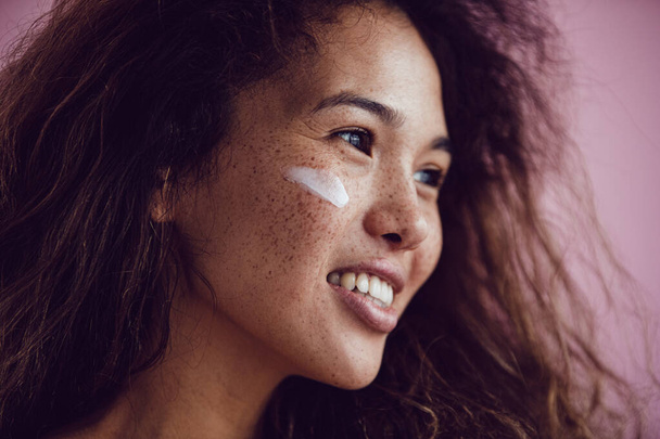 Portrait of a woman with curly hair and freckles with cream on her face. - Foto, afbeelding