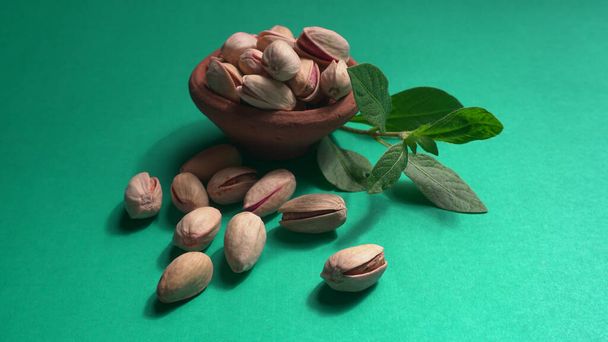 Pistachios or Pista nuts decorated with green leaves and brown bowl. Green background, top view. Flat lay. - Foto, Imagem