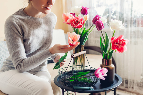 Woman arranges bouquet of tulips flowers at home. Housewife enjoys blooms in vases on table. Interior and decor - Foto, Imagen