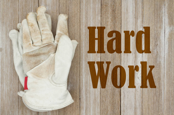 Mensaje de trabajo duro con guantes de trabajo de cuero recubiertos de suciedad en madera envejecida - Foto, Imagen