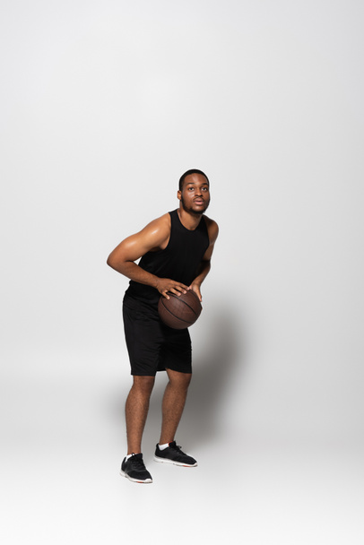 full length of african american player holding basketball while aiming on grey - Photo, Image