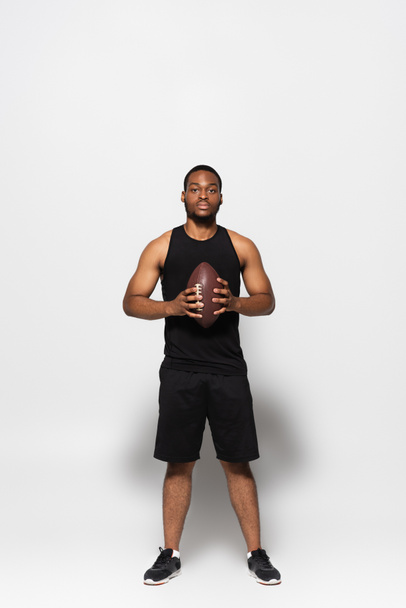 full length of african american sportsman holding rugby ball on grey  - Photo, Image