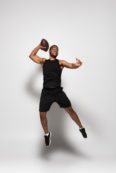 longitud completa de deportista afroamericano jugando rugby y saltando sobre gris  - Foto, imagen