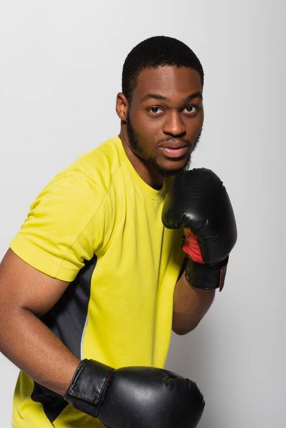 fuerte afroamericano deportista haciendo ejercicio en guantes de boxeo aislado en gris - Foto, Imagen