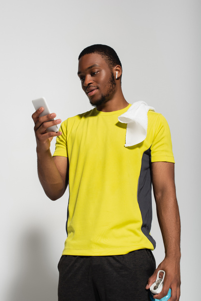 african american sportsman with earphone in ear using smartphone on grey - Photo, Image