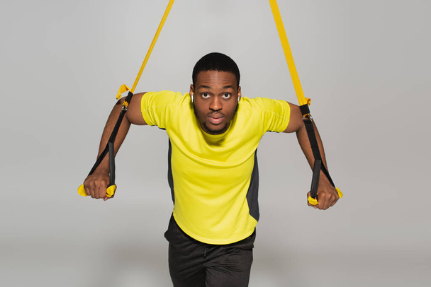 strong african american sportsman exercising with resistance bands on grey - Foto, afbeelding