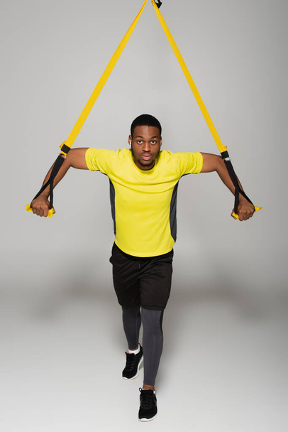 longitud completa en fuerte afroamericano deportista ejerciendo con bandas de resistencia en gris - Foto, imagen