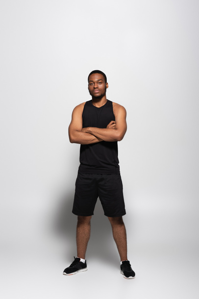 full length of african american sportsman in tank top and shorts standing with crossed arms on grey - Valokuva, kuva