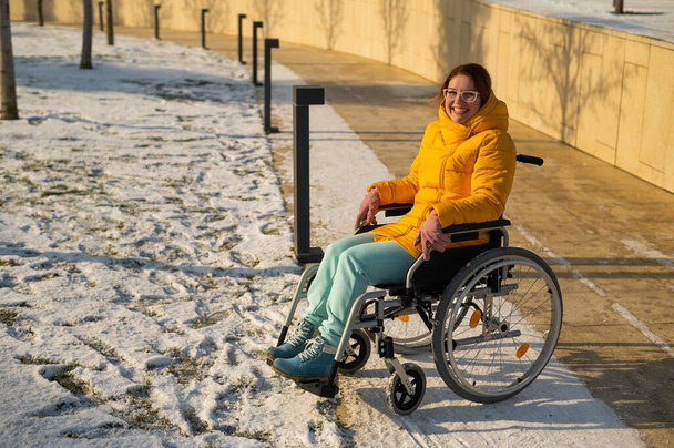 Caucasian woman with disabilities rides on a chair in the park in winter. Girl on a walk in a wheelchair.  - Foto, afbeelding