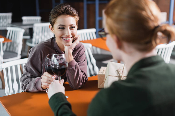 Pareja joven brindando con vino cerca de regalos en la cafetería del hotel  - Foto, imagen