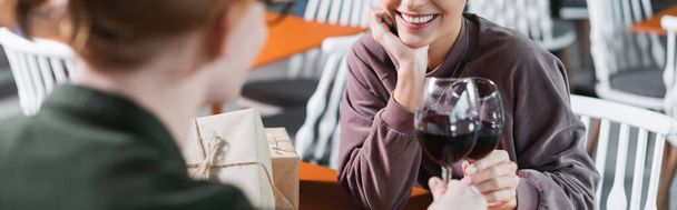 Обрізаний вид усміхненої пари тостів вина біля подарунків у готельному кафе, банер
  - Фото, зображення