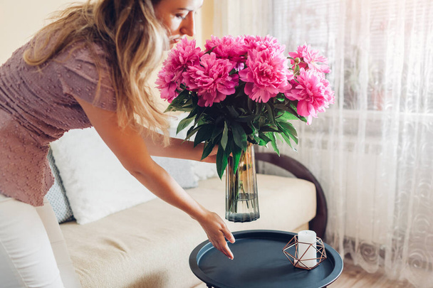 Frau stellt Vase mit Pfingstrosen-Blumen auf den Tisch. Hausfrau sorgt für Gemütlichkeit zu Hause. Interieur und Feder Dekor - Foto, Bild