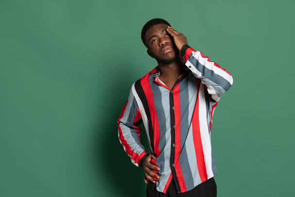 One young stylish african man wearing bright striped shirt and jeans isolated on green studio background. Emotions, facial expression concept. - Foto, immagini