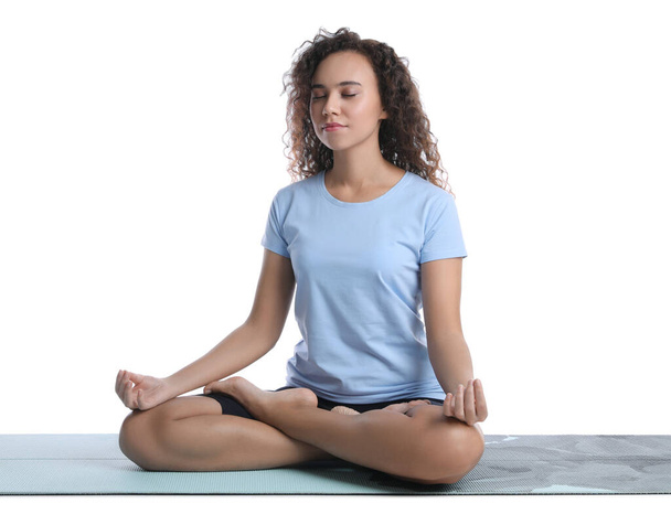 Beautiful African-American woman meditating on yoga mat against white background - Фото, изображение