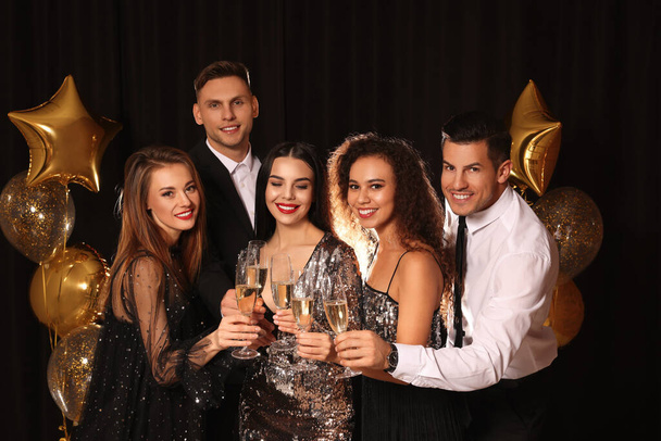Happy friends with glasses of sparkling wine celebrating New Year on black background - Fotografie, Obrázek