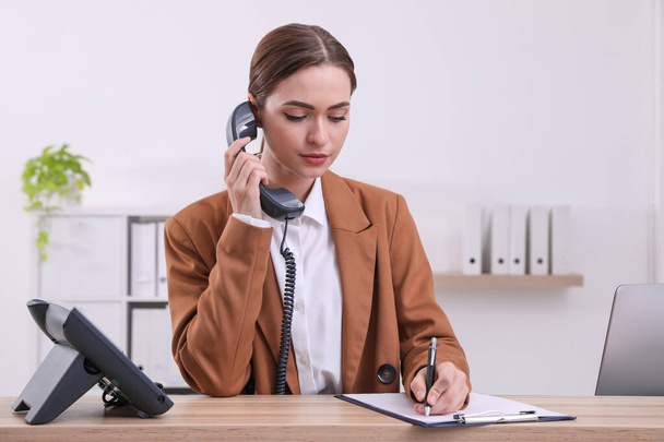 Female receptionist with clipboard talking on phone at workplace - Фото, зображення