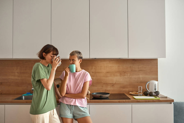 Lesbian couple drinking tea or coffee at kitchen - Valokuva, kuva