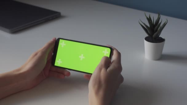 Schermo verde a chiave cromatica orizzontale su smartphone in mani sottili su tavolo bianco - Filmati, video