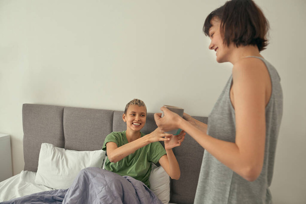 Girl giving cup with tea to her girlfriend in bed - Foto, imagen
