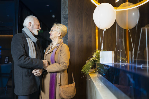 Elderly couple standing together in front of a hotel reception - Zdjęcie, obraz
