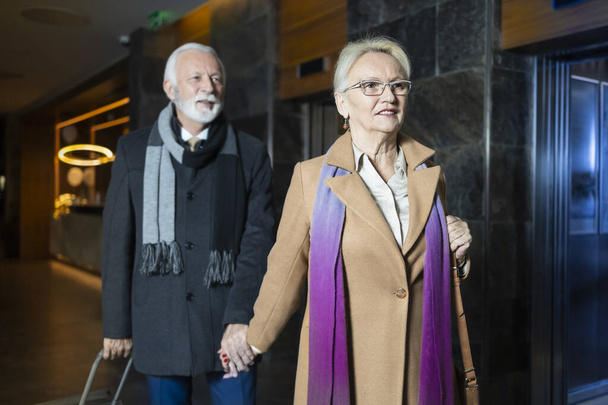 Az idősebb feleség és a férj együtt érkeznek egy hotel előcsarnokába Valentin-napi nyaralásukra. - Fotó, kép