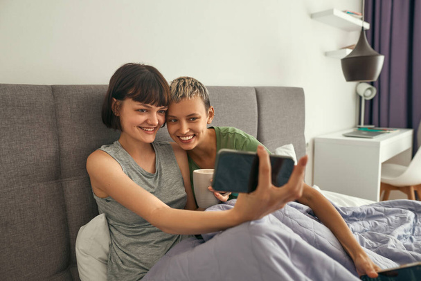 Lesbians take selfie on smartphone on bed at home - 写真・画像