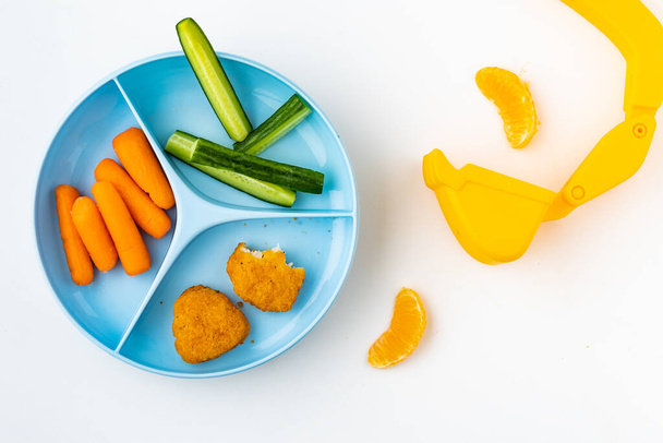 Hračkový bagr umístěný vedle zdravé dětské stravy obsahující plátky okurek, mrkve, kuřecí nugety a kousky mandarinek - Fotografie, Obrázek