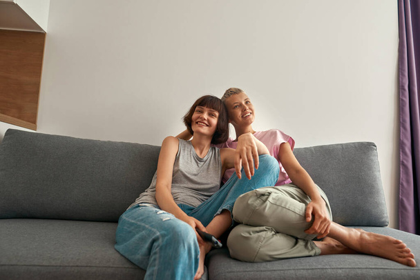 Young smiling lesbian girls watching TV on sofa - Foto, afbeelding