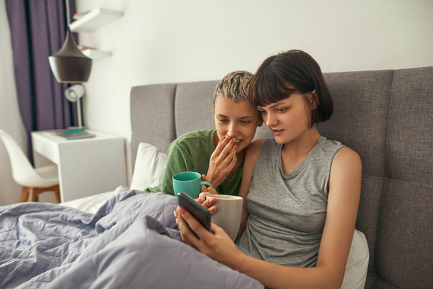Young lesbians watching on smartphone on bed - Fotografie, Obrázek