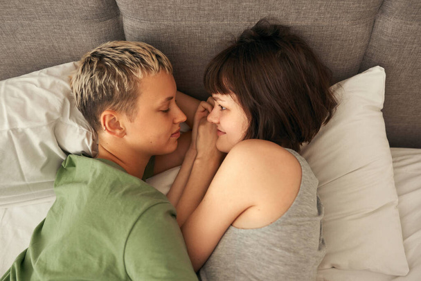 Young caucasian lesbian couple rest on bed at home - Фото, изображение