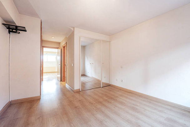 Bedroom with built-in wardrobe and mirrored doors with light wooden floor - Fotó, kép
