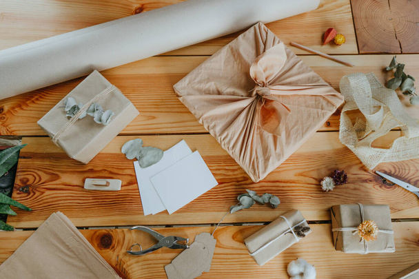 Emballage des boîtes-cadeaux en tissu (furoshiki) et du papier artisanal avec des fleurs séchées sur la table. Concept de paquet écologique. Vue de dessus, plan plat. - Photo, image