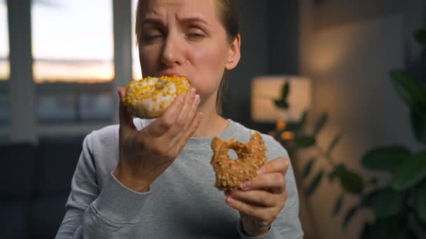 Binge syö käsite. Valkoihoinen nainen, jolla on syömishäiriö syö kaksi donitsia nopeasti ja samaan aikaan. - Materiaali, video