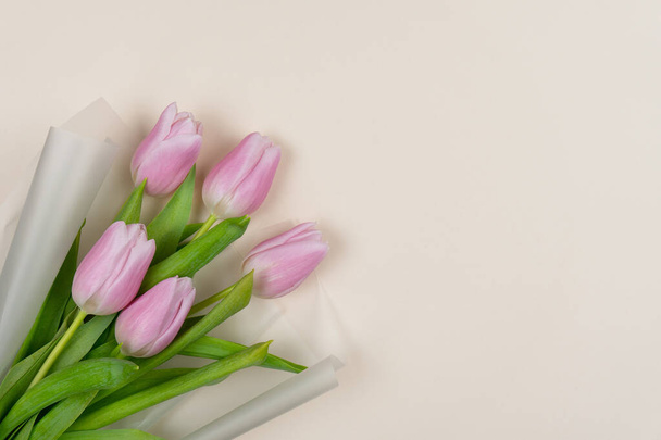 Bouquet of pink tulips in translucent matte white paper on a beige background. Valentine's Day, International Women's Day, Mother's Day, Birthday, Anniversary, Easter. Copy space - Foto, Imagen