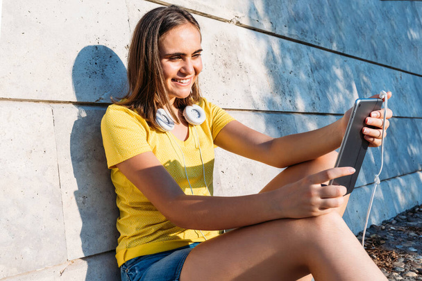 Young blond hair girl wearing yellow t-shirt and white headphones, smiling and looking at her tablet. Technology, lifestyle and relaxation concept - Фото, зображення