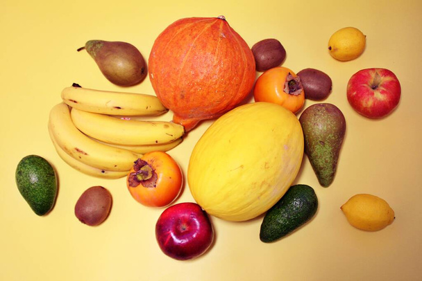colorful fruits, fruits scattered on a yellow background, sharon, yellow melon, pear, bananas, kiwi, avocado, fresh vitamins - Photo, Image