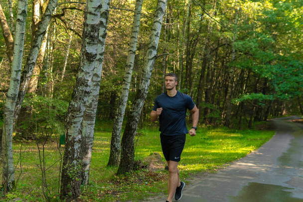 A man athlete runs in the park outdoors, around the forest, oak trees green grass young enduring athletic athlete active sport exercise, lifestyle jogger training wellness jog, park wellbeing. body - Foto, immagini