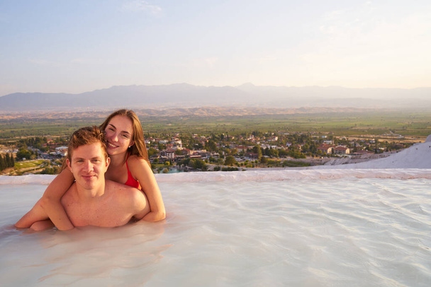 Loving couple at swimming pool in Pamukkale - St.Valentines Day concept.Lovers at sunset enjoing beautiful mountains view on their romantic journey.                                                - Foto, imagen