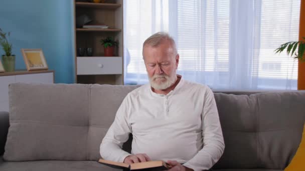 bolest zad u starších mužů čtení knihy na pohovce, nezdravý starý šedovlasý muž dotkne bolavé dolní části zad - Záběry, video