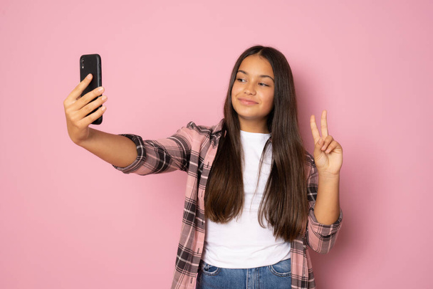 Happy beautiful young girl with long hair using mobile phone over pink background - Фото, изображение